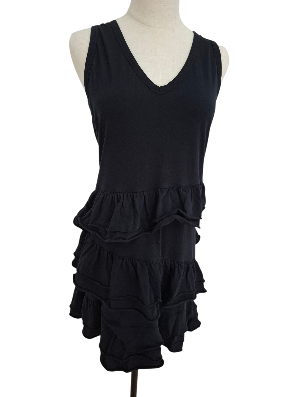 A black sleeveless V-neck dress displayed on a cream mannequin torso against a plain white background. The dress features a solid upper bodice and a tiered ruffle skirt.