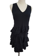 A black sleeveless V-neck dress displayed on a cream mannequin torso against a plain white background. The dress features a solid upper bodice and a tiered ruffle skirt.