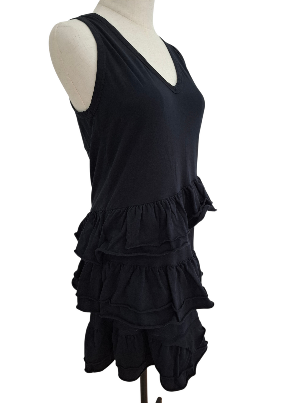 A black sleeveless V-neck top with a tiered ruffle hem, displayed on a cream mannequin torso against a plain white background.