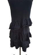 A black sleeveless dress displayed on a dress form mannequin against a plain white background. The dress features a tiered ruffle hem.
