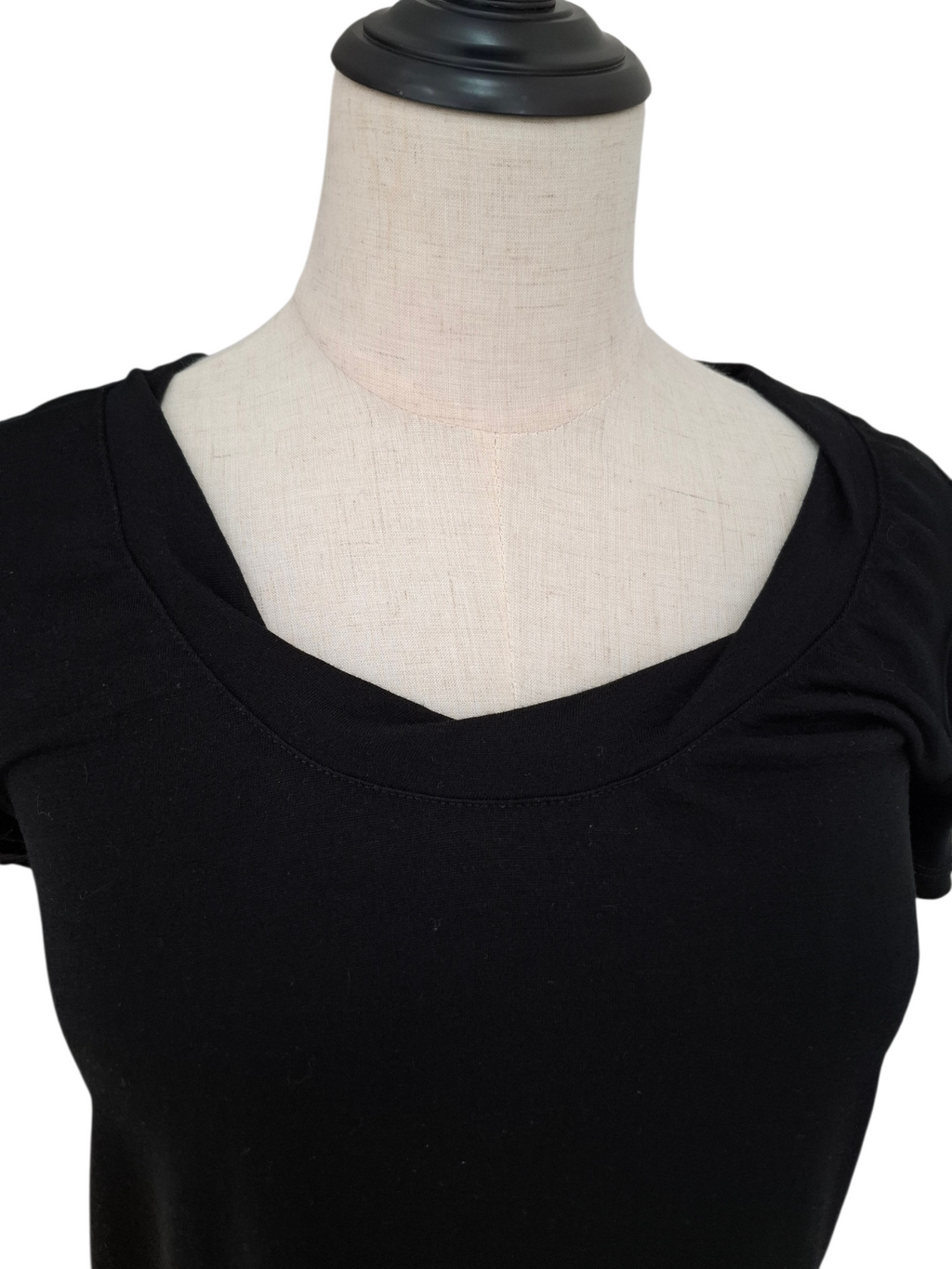 A close-up of a black short-sleeve scoop-neck top displayed on a cream fabric dress form mannequin against a white background.