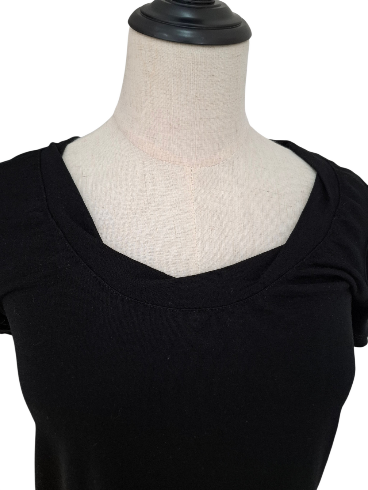 A close-up of a black short-sleeve scoop-neck top displayed on a cream fabric dress form mannequin against a white background.