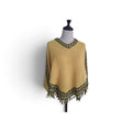 A mustard yellow knit poncho sweater with black and gold patterned trim and fringe, displayed on a mannequin torso against a white background.
