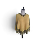 A mustard yellow knit poncho sweater with black and gold patterned trim and fringe, displayed on a mannequin torso against a white background.