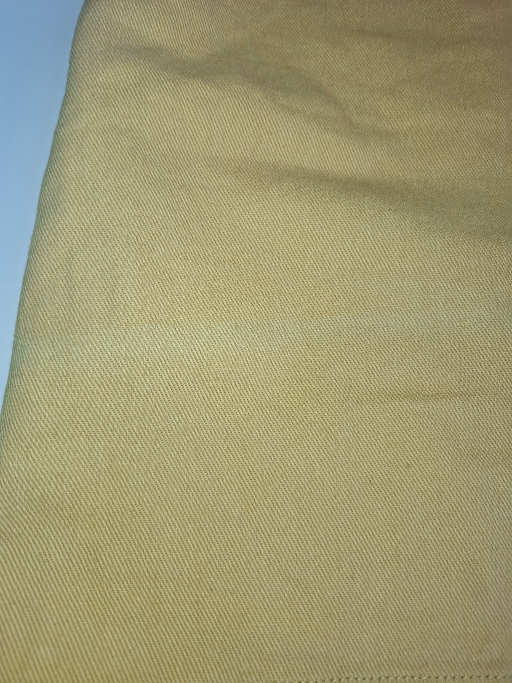 A close-up of a light tan or beige textured fabric, showing a fine diagonal twill weave pattern.