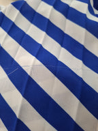 A close-up of a blue and white diagonally striped fabric with visible folds and a small loose thread on the surface.