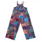 A pair of patchwork-print wide-leg pants with thin shoulder straps, featuring a colorful collage of various patterns including paisley, stripes, and geometric shapes in blue, red, pink, yellow, and black on a white background.