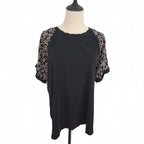 A black short-sleeve top with beige floral lace sleeves, displayed on a mannequin torso against a white background.