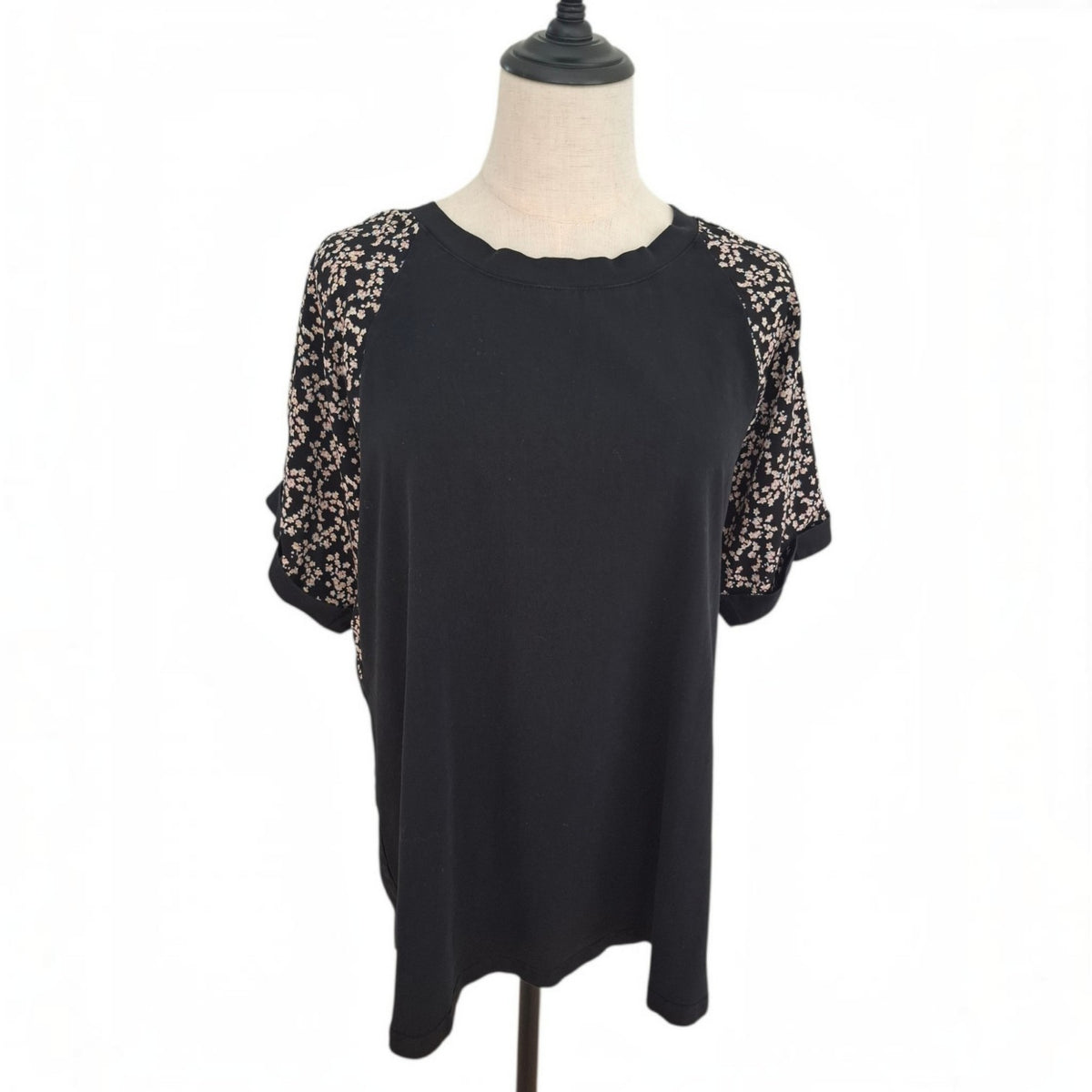 A black short-sleeve top with beige floral lace sleeves, displayed on a mannequin torso against a white background.