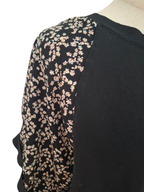 Close-up of a black raglan-style top on a mannequin, featuring a black sleeve with a dense small floral print in pale pink, peach, and cream tones.