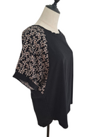 A black short-sleeve top with sheer floral-patterned sleeves, displayed on a cream dress form against a white background.