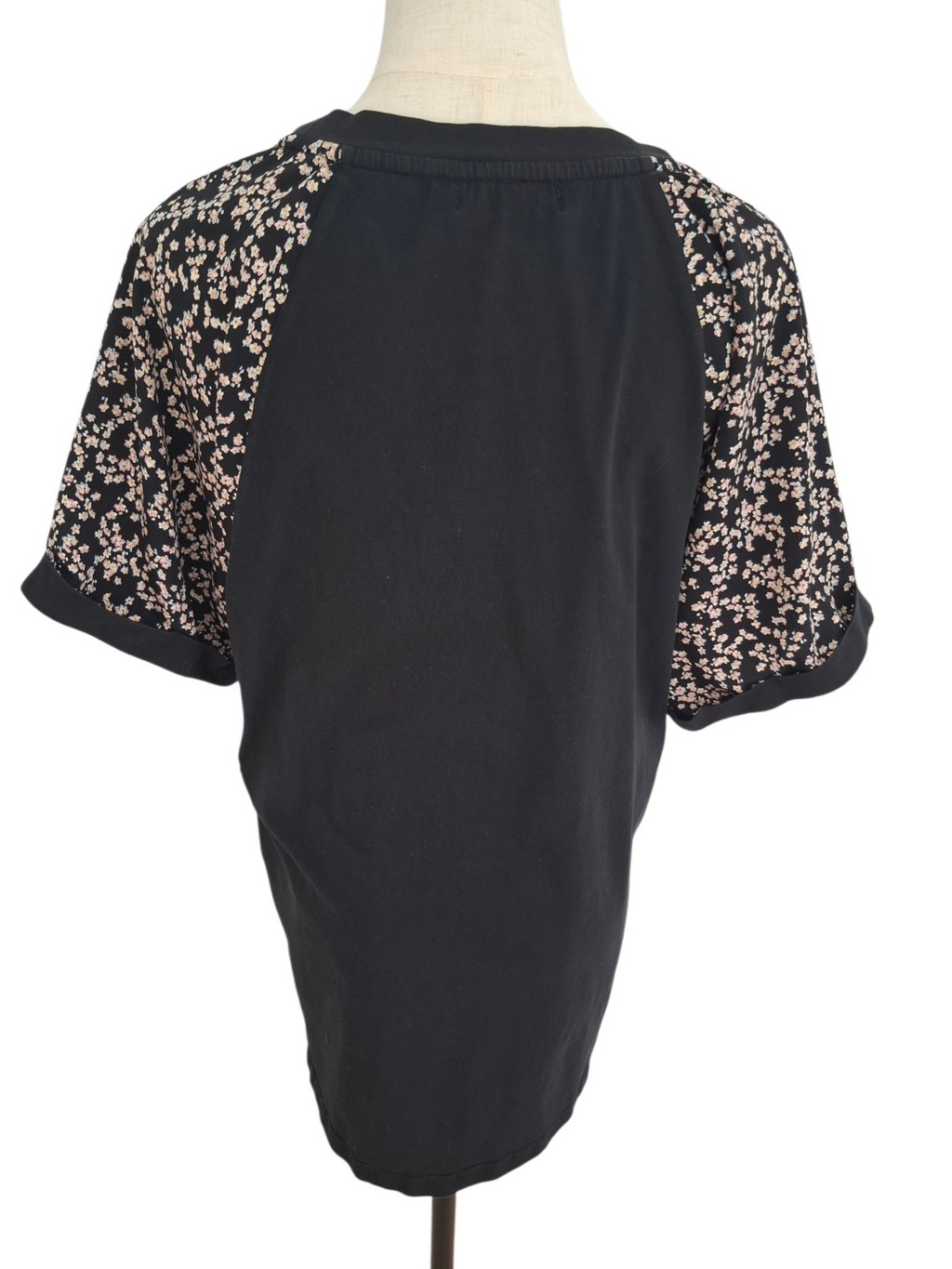 A black short-sleeve top displayed on a mannequin torso, featuring beige and black floral lace raglan sleeves.