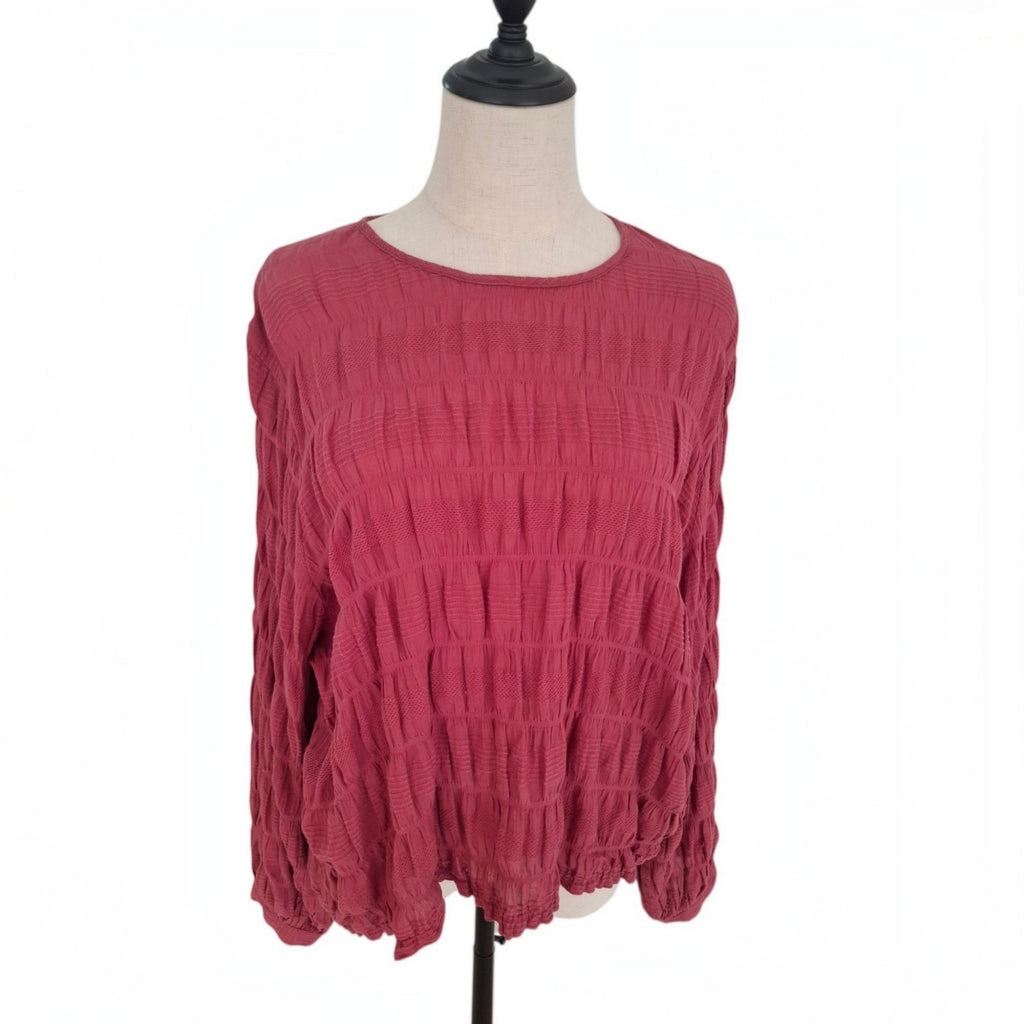A dusty rose pink long-sleeve blouse with a textured crinkled fabric, displayed on a dress form