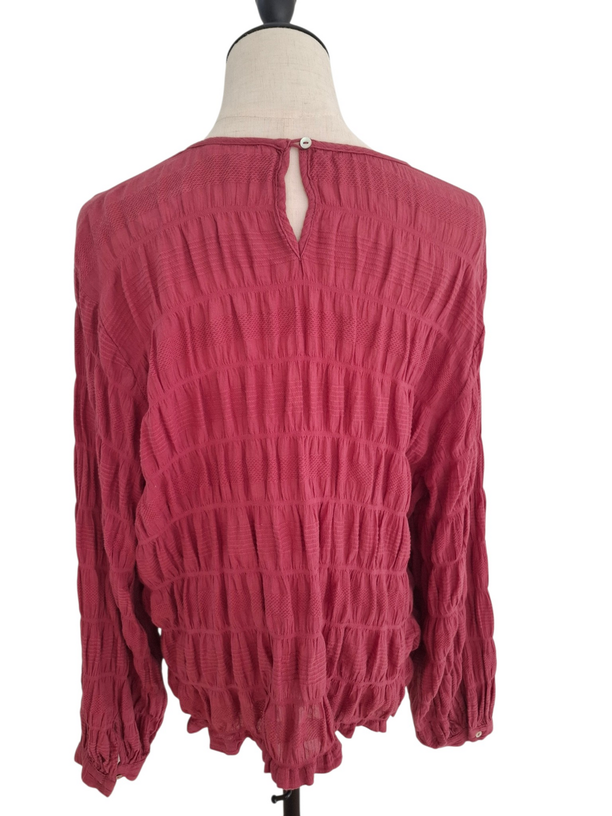 A dusty rose pink long-sleeve blouse with a textured crinkled fabric, displayed on a dress form mannequin against a white background.