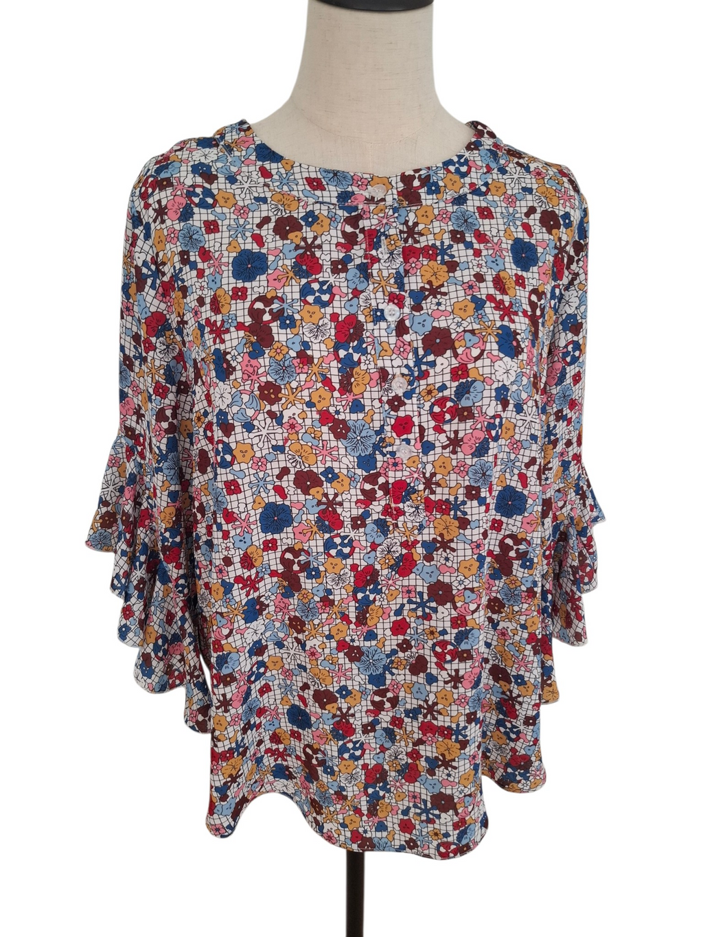 A women's long-sleeve blouse with a dense multicolor floral and abstract print, displayed on a dress form mannequin against a white background.
