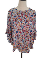 A women's long-sleeve blouse with a dense multicolor floral and abstract print, displayed on a dress form mannequin against a white background.