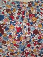 A close-up of a colorful floral fabric with a white grid background and multicolored flowers, featuring white buttons sewn along the front.