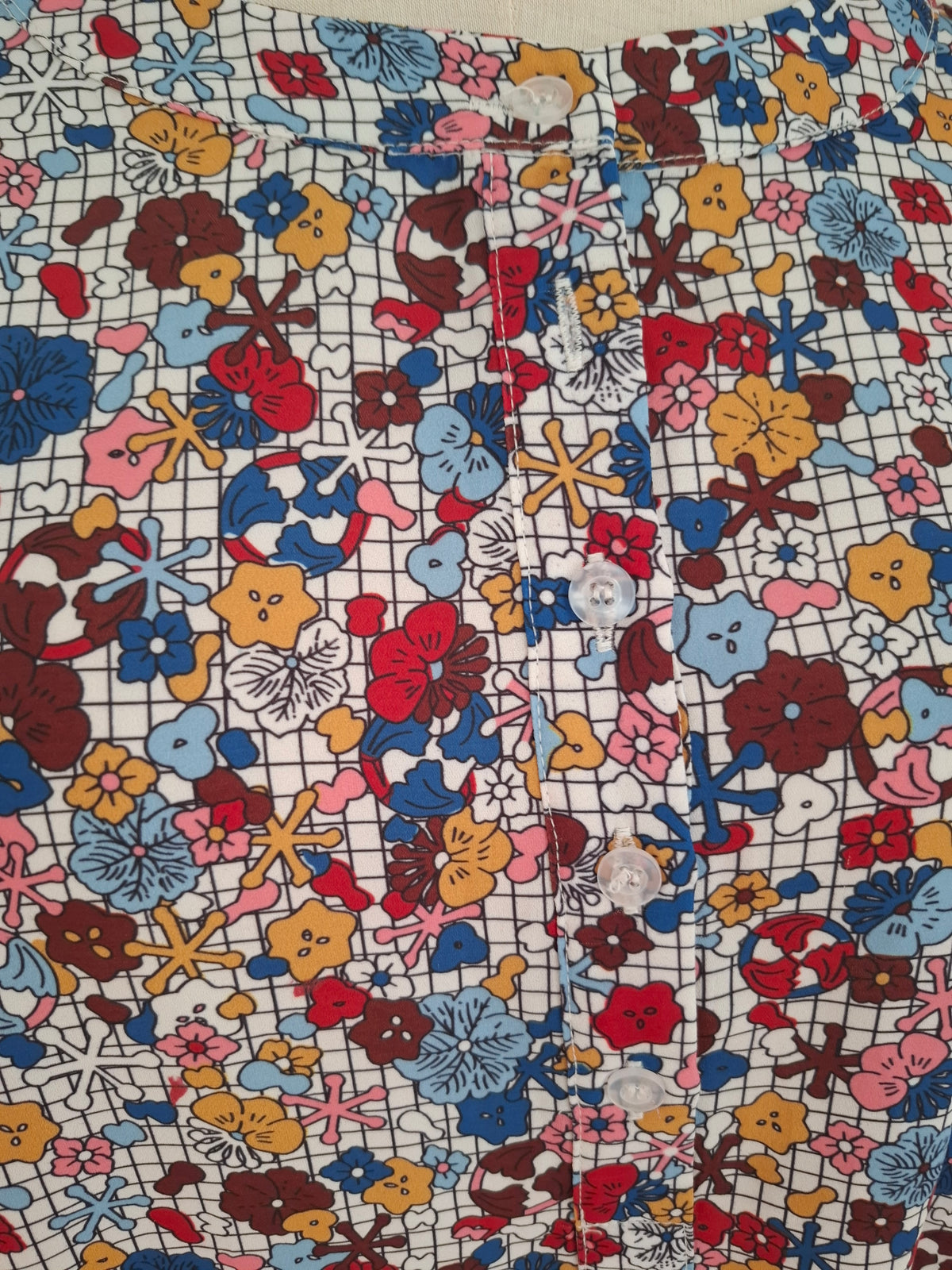 A close-up of a colorful floral fabric with a white grid background and multicolored flowers, featuring white buttons sewn along the front.