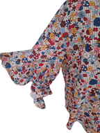 A close-up of a long-sleeve blouse with a ruffled cuff and a dense multicolor floral print on a white base, shown against a plain white background.