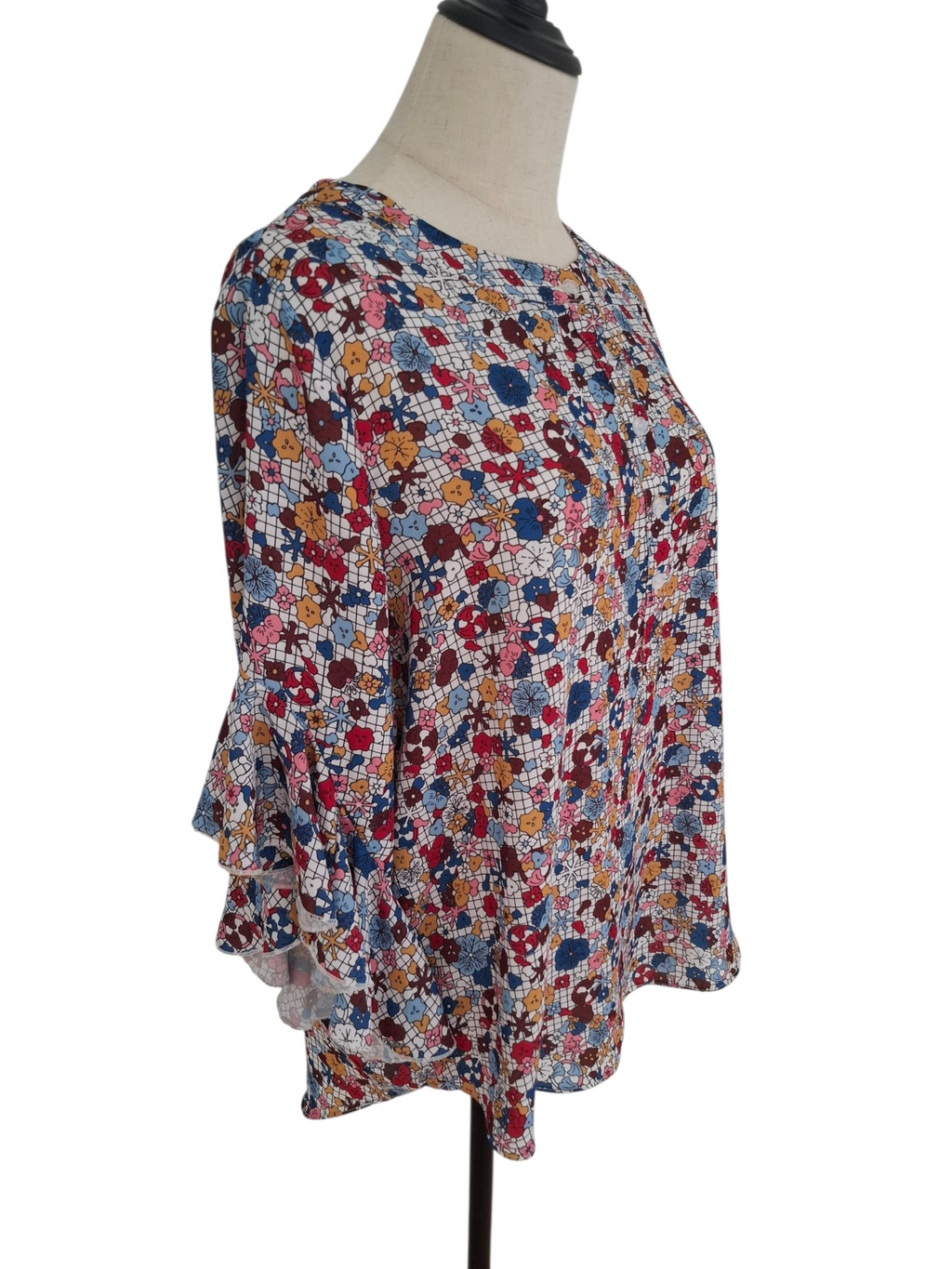 A women's long-sleeve blouse with a dense multicolor floral and geometric print, displayed on a dress form mannequin against a white background.
