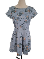 A short-sleeve fit-and-flare dress on a mannequin, featuring a dusty blue-gray base with an all-over floral print in orange, white, and dark green.
