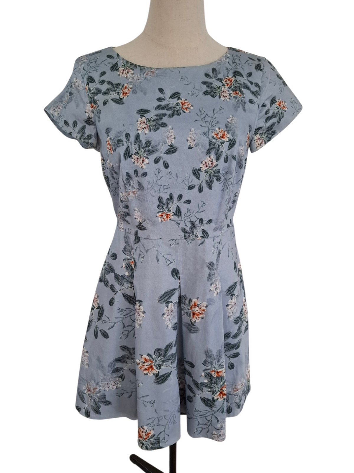 A short-sleeve fit-and-flare dress on a mannequin, featuring a dusty blue-gray base with an all-over floral print in orange, white, and dark green.