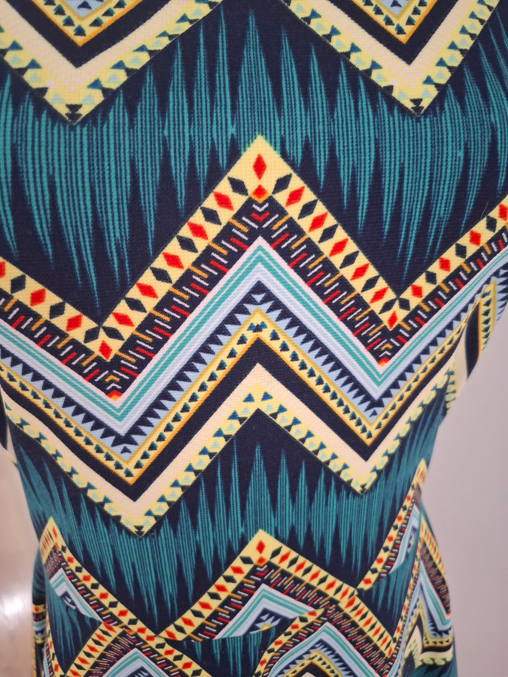 A close-up of a garment featuring a bold geometric chevron pattern in teal, navy, cream, yellow, and red.