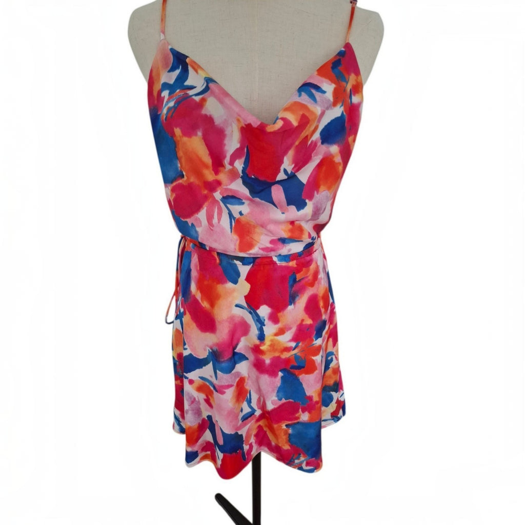 A sleeveless wrap-style mini dress with thin straps and a drawstring waist, featuring a vibrant abstract floral print in pink, red, orange, and blue, displayed on a beige mannequin torso against a white background.