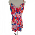 A sleeveless wrap-style mini dress with thin straps and a drawstring waist, featuring a vibrant abstract floral print in pink, red, orange, and blue, displayed on a beige mannequin torso against a white background.