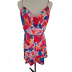 A sleeveless wrap-style mini dress with thin straps and a drawstring waist, featuring a vibrant abstract floral print in pink, red, orange, and blue, displayed on a beige mannequin torso against a white background.
