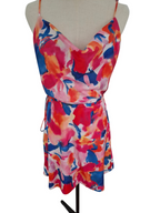 A sleeveless wrap-style mini dress with thin straps and a self-tie waist, featuring a vibrant abstract floral print in red, pink, orange, and blue, displayed on a beige mannequin torso against a white background.