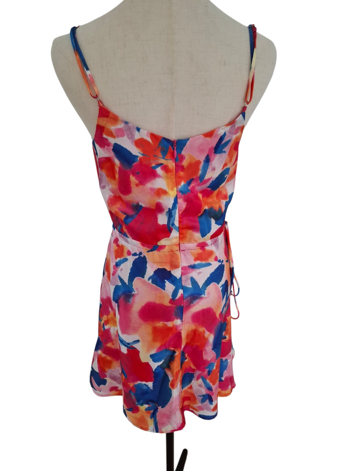 A sleeveless floral print mini dress with thin shoulder straps and a side tie, displayed on a beige fabric mannequin torso against a white background.