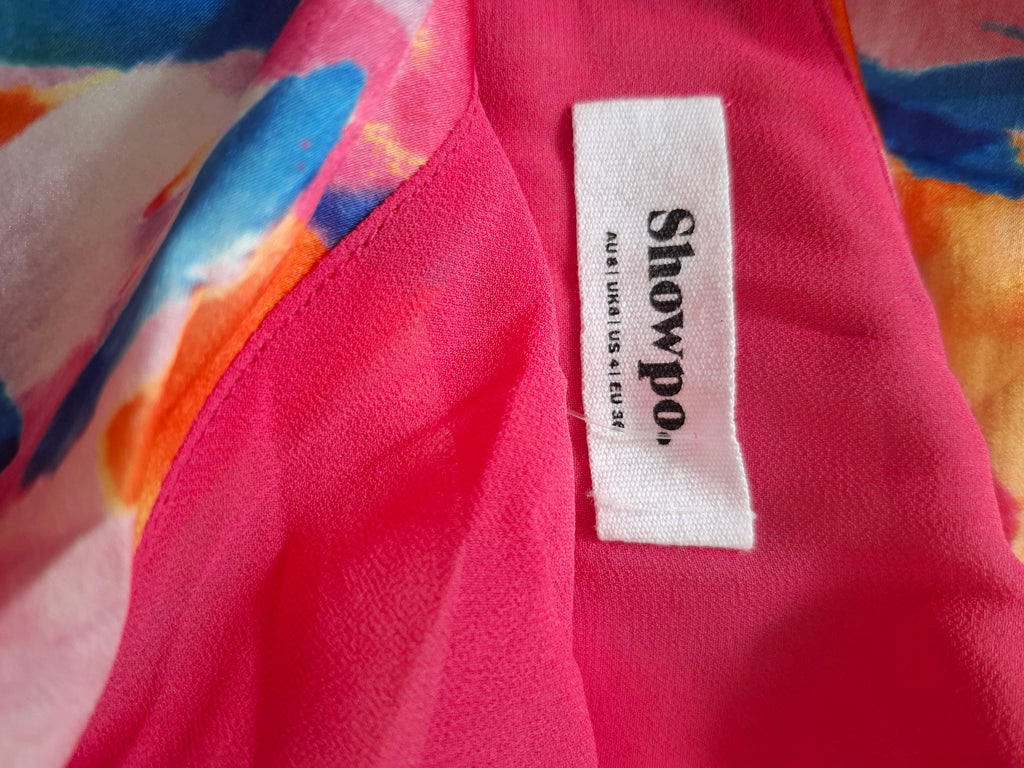 Close-up of a bright pink garment with a white fabric brand label reading 'Showpo.' and smaller text 'Aloha USA 41 US 23'.