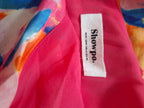 Close-up of a bright pink garment with a white fabric brand label reading 'Showpo.' and smaller text 'Aloha USA 41 US 23'.