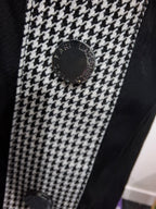 Close-up of a black and white houndstooth patterned garment with a round black button engraved with 'FARL LONDON'.
