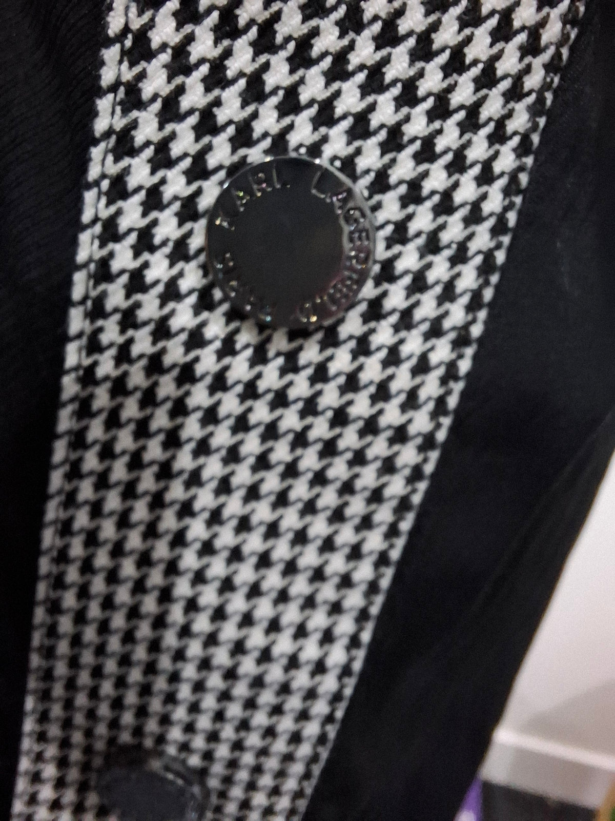 Close-up of a black and white houndstooth patterned garment with a round black button engraved with 'FARL LONDON'.