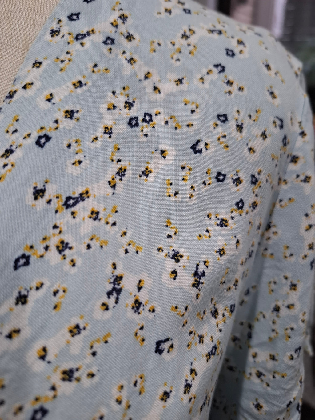 A close-up of a light blue knit fabric with a small-scale abstract floral or ikat pattern in navy blue, mustard yellow, and off-white.