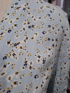 A close-up of a light blue knit fabric with a small-scale abstract floral or ikat pattern in navy blue, mustard yellow, and off-white.