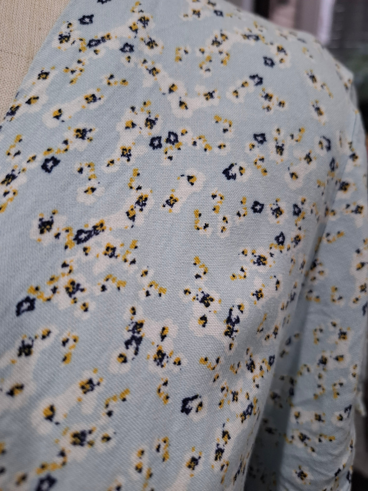 A close-up of a light blue knit fabric with a small-scale abstract floral or ikat pattern in navy blue, mustard yellow, and off-white.
