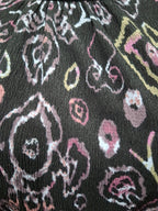 A close-up of a black fabric with a distressed, ikat-style floral pattern in pink, white, and yellow.