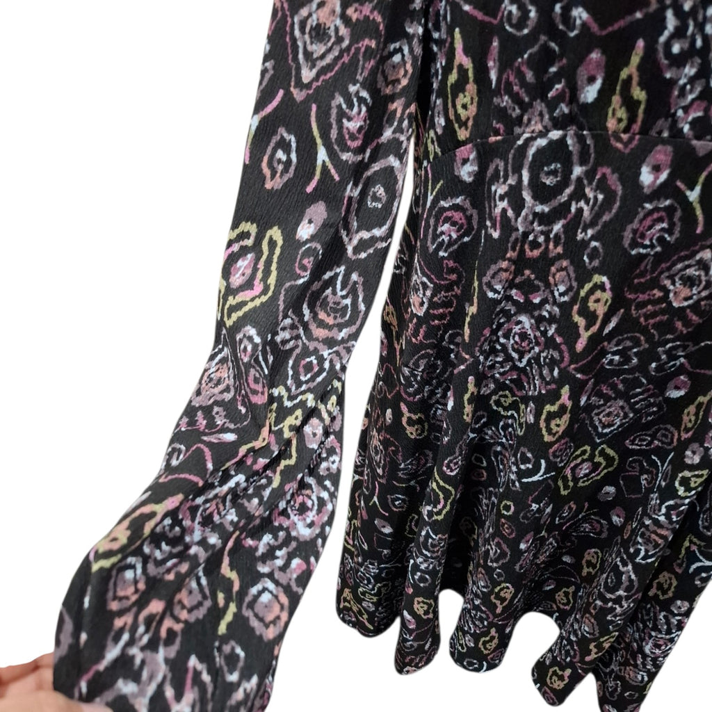 A close-up of a black long-sleeve blouse with a colorful abstract floral pattern in pink, yellow, and white, featuring gathered cuffs and a ruffled hem.