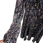 A close-up of a black long-sleeve blouse with a colorful abstract floral pattern in pink, yellow, and white, featuring gathered cuffs and a ruffled hem.