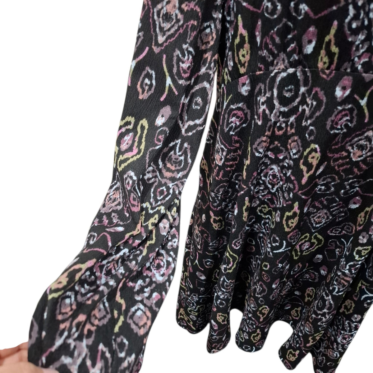 A close-up of a black long-sleeve blouse with a colorful abstract floral pattern in pink, yellow, and white, featuring gathered cuffs and a ruffled hem.