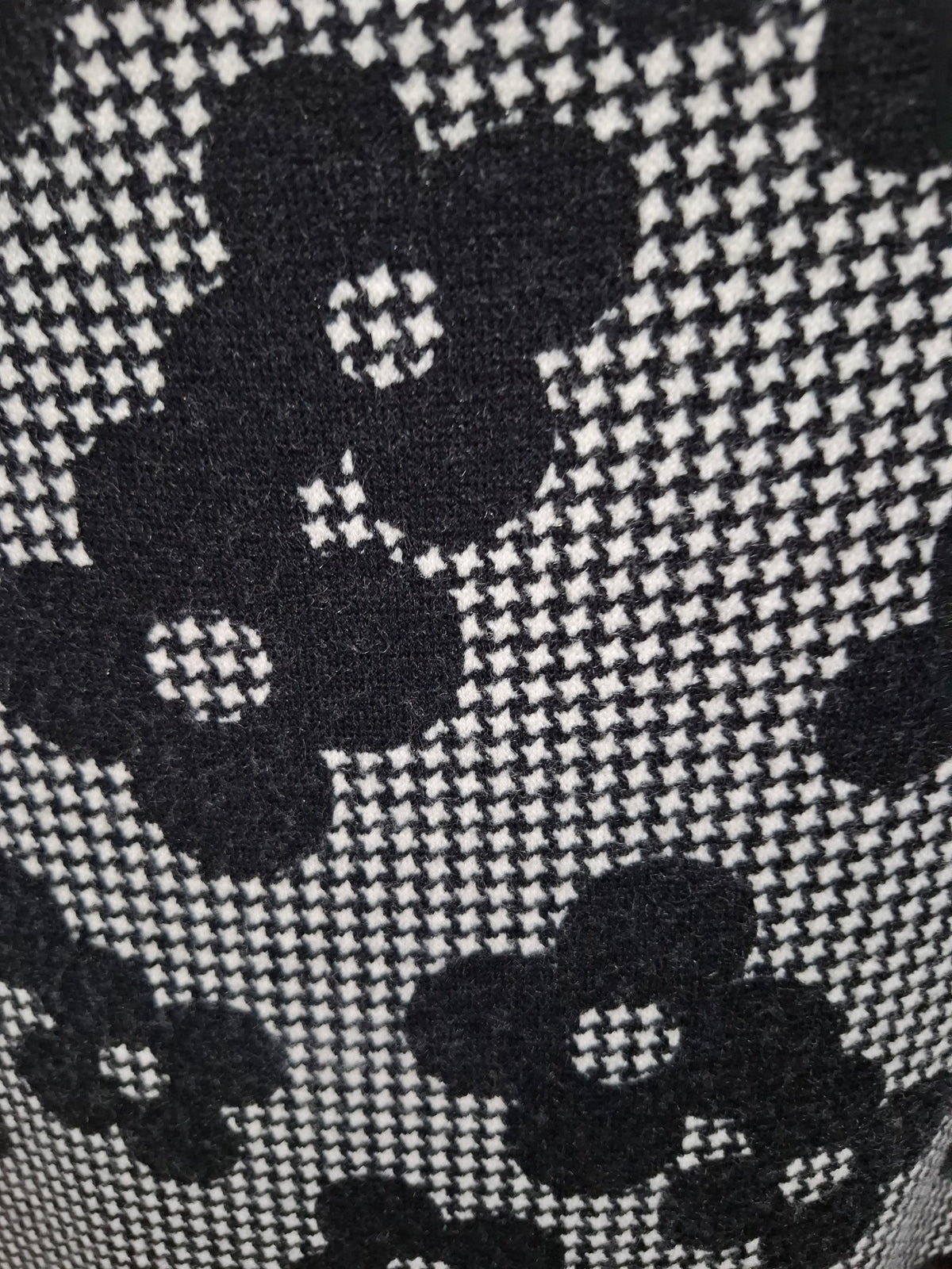 Close-up of a black and white woven fabric pattern featuring large floral motifs over a fine houndstooth background.