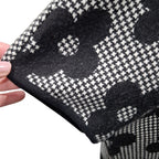 A close-up of a black and white patterned knit fabric being held by a hand, showing a textured houndstooth-like weave with large abstract floral shapes.