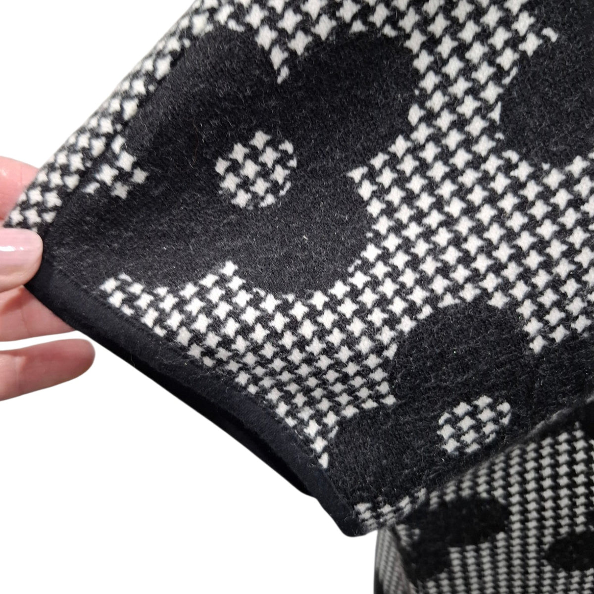A close-up of a black and white patterned knit fabric being held by a hand, showing a textured houndstooth-like weave with large abstract floral shapes.