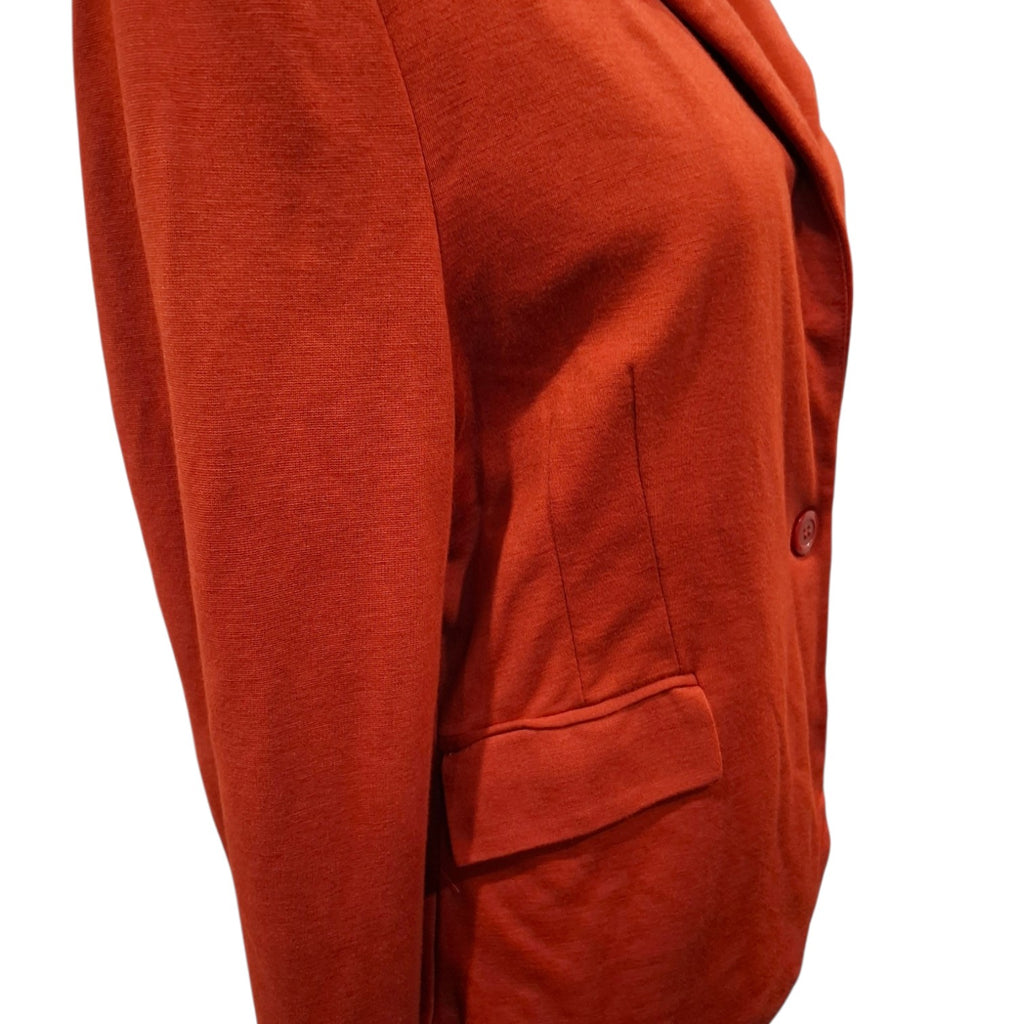 Close-up of a rust-orange blazer or cardigan sleeve and body section, showing a single button closure and a welt pocket, photographed against a plain white background.