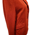 Close-up of a rust-orange blazer or cardigan sleeve and body section, showing a single button closure and a welt pocket, photographed against a plain white background.