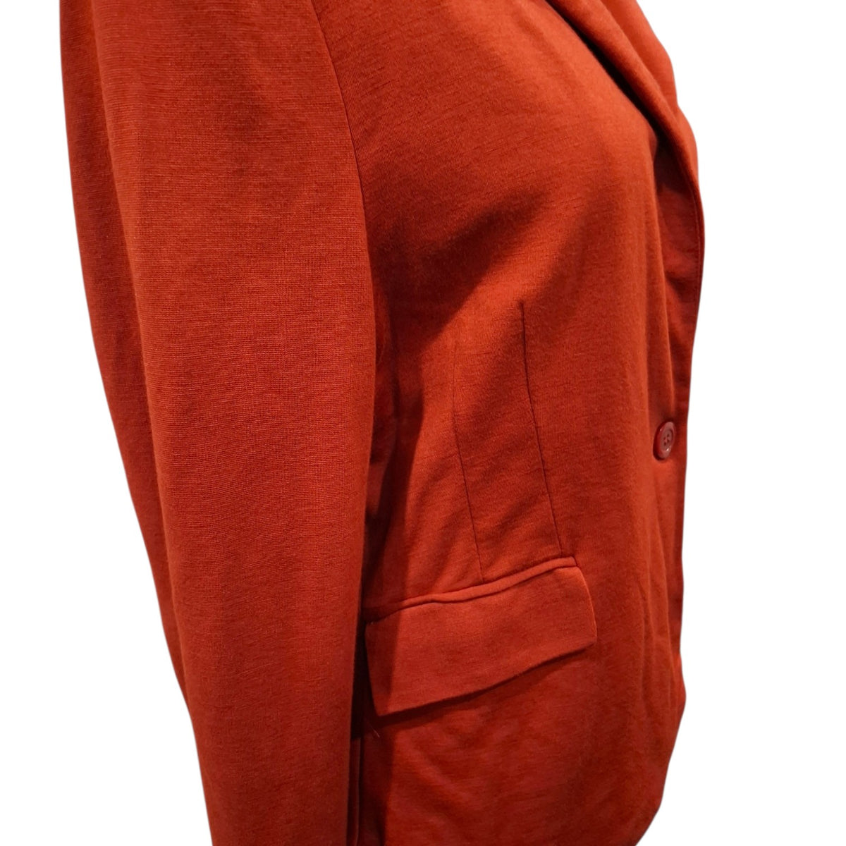 Close-up of a rust-orange blazer or cardigan sleeve and body section, showing a single button closure and a welt pocket, photographed against a plain white background.