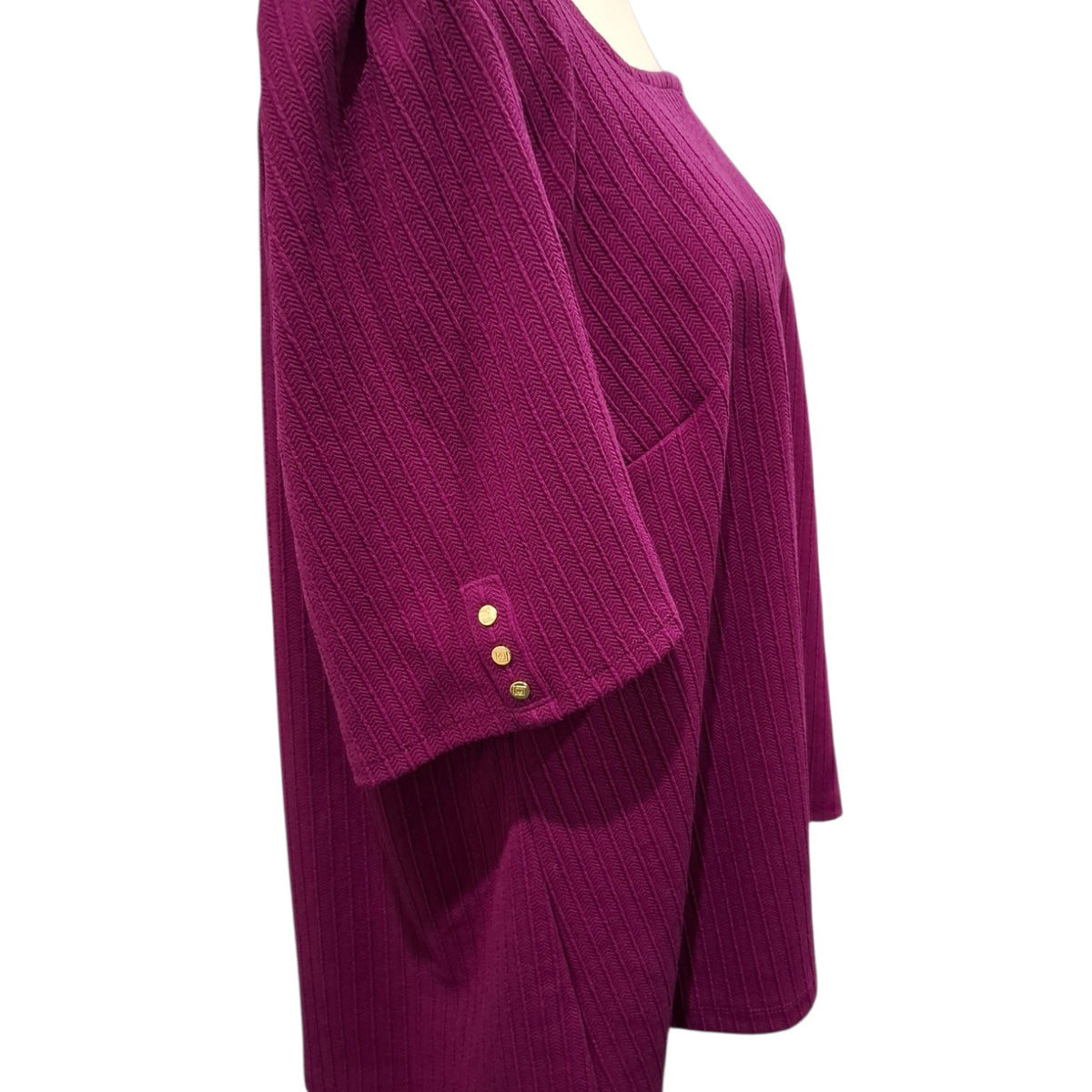 A close-up side view of a magenta ribbed knit top on a mannequin, featuring three gold buttons on the sleeve cuff.